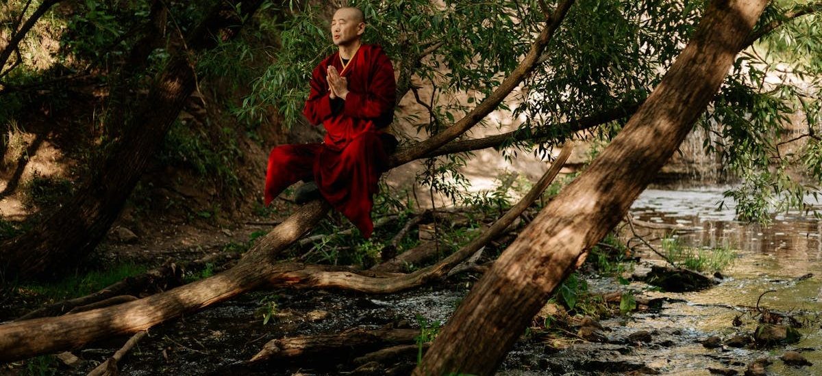A serene monk in red robes meditates by a forest stream, embracing nature's tranquility.