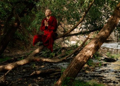 A serene monk in red robes meditates by a forest stream, embracing nature's tranquility.